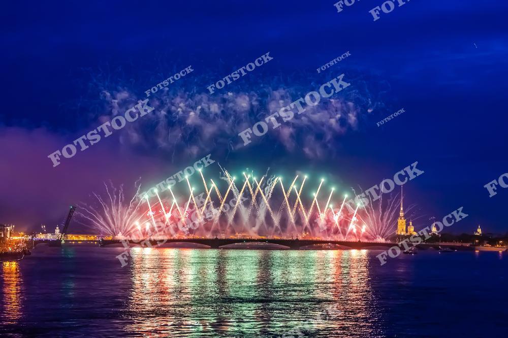 На фотографии изображен грандиозный фейерверк, освещающий ночное небо Санкт-Петербурга. На заднем плане виднеется Петропавловская крепость с высокой шпилем колокольни.